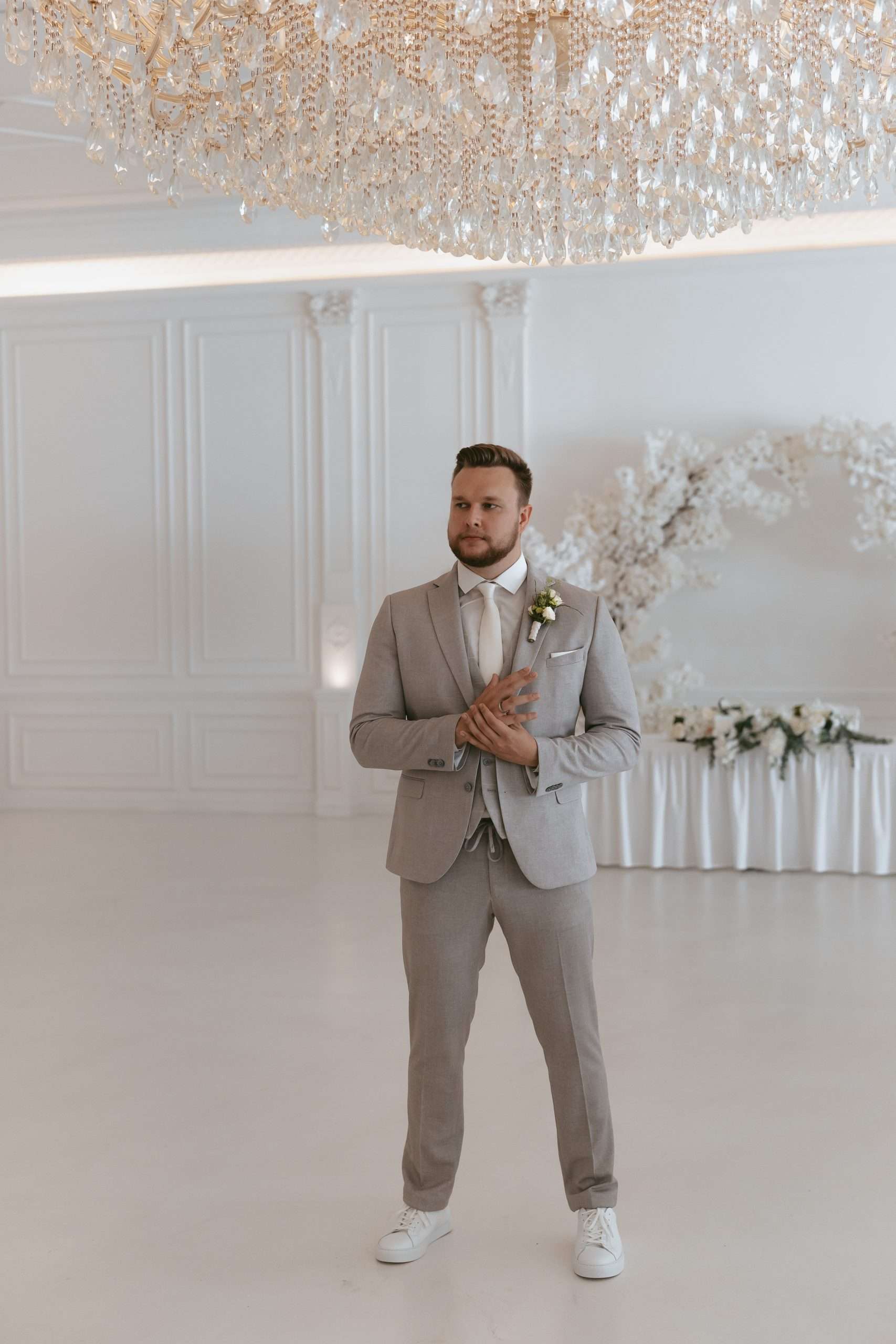 Ein Mann vor einer Hochzeit in einem beigen Anzug mit weißem Hemd und weißer Krawatte hält sich seinen Ehering.